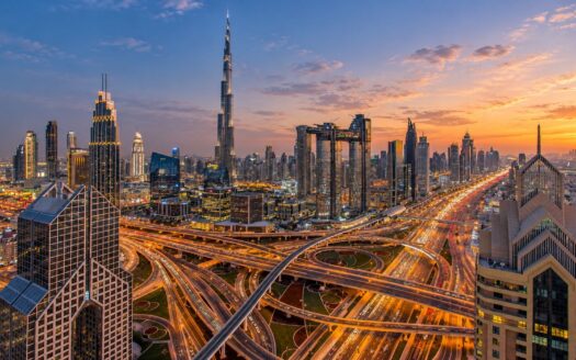 Dubai skyline at twilight with the Burj Khalifa above a glowing highway interchange and light trails from traffic
